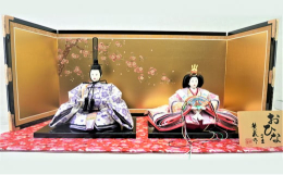 おひな様の御衣裳は京都西陣織金襴の桜柄色違いで制作しました。おひな様だけをシンプルに飾るタイプで、敷物は桜柄入りの赤金襴にし、可愛く飾り付けしました。金箔に枝桜を施した屏風がおひな様の御衣裳を更に引き
